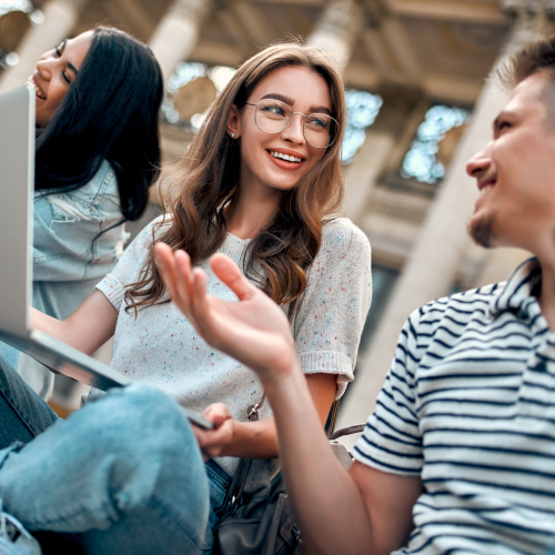 Image of young college students chatting while working on laptops, representing the target audience for the RoboCode project.